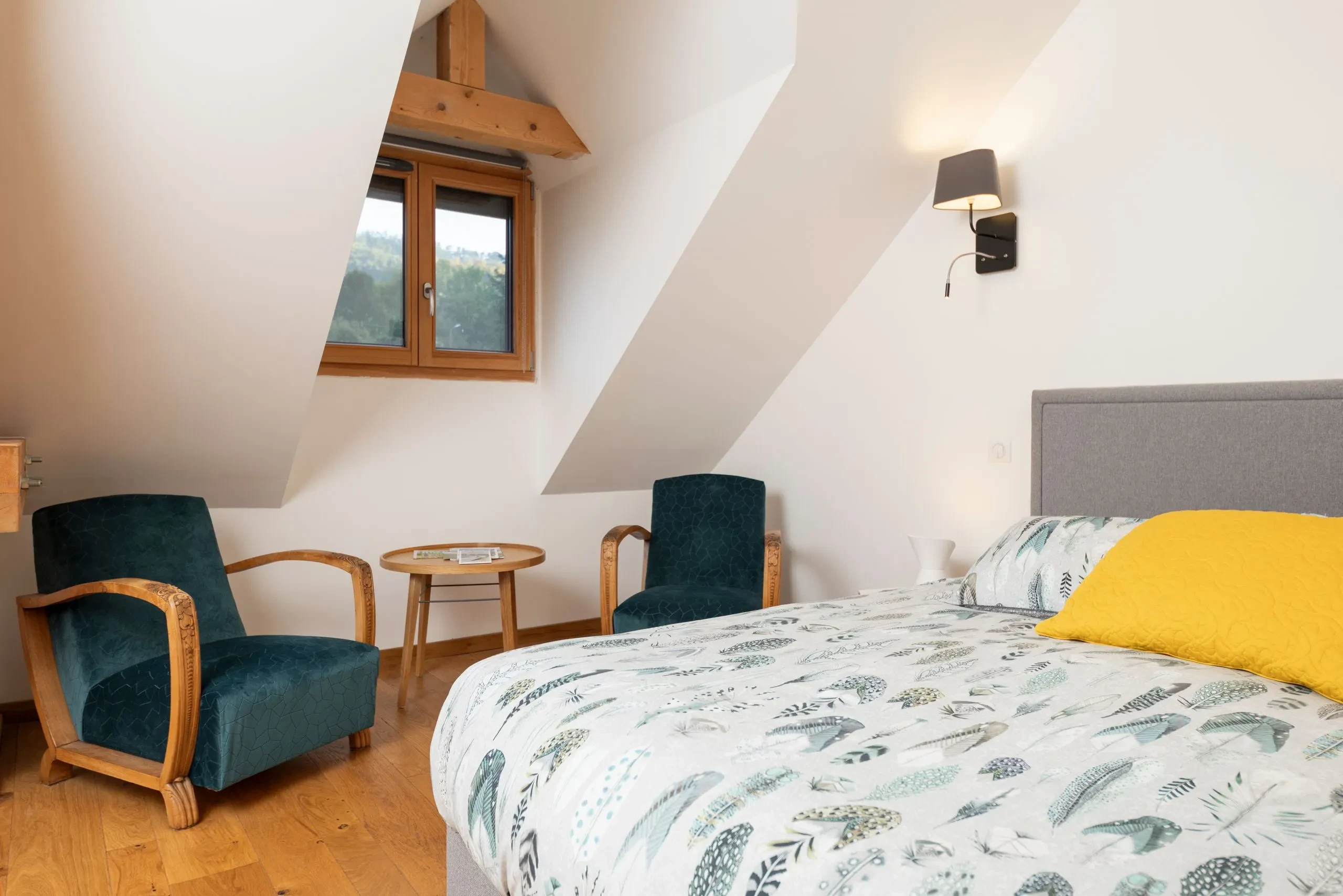 Chambre mansardée avec lit et fauteuils en bois
