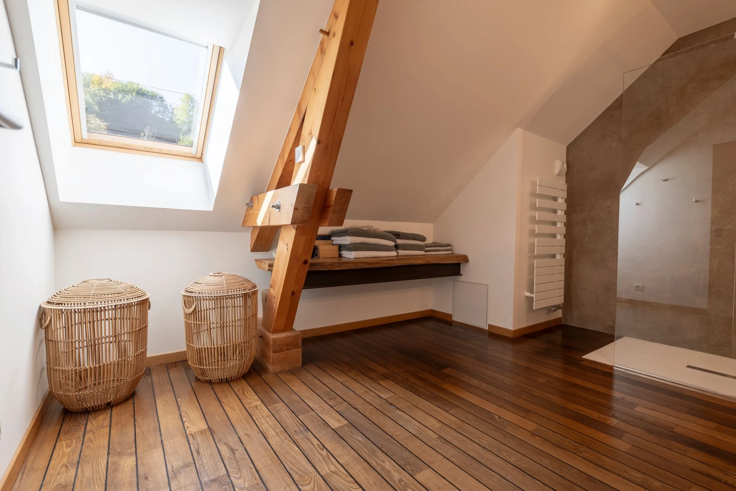 Salle de bain mansardée avec parquet et verrière de douche.