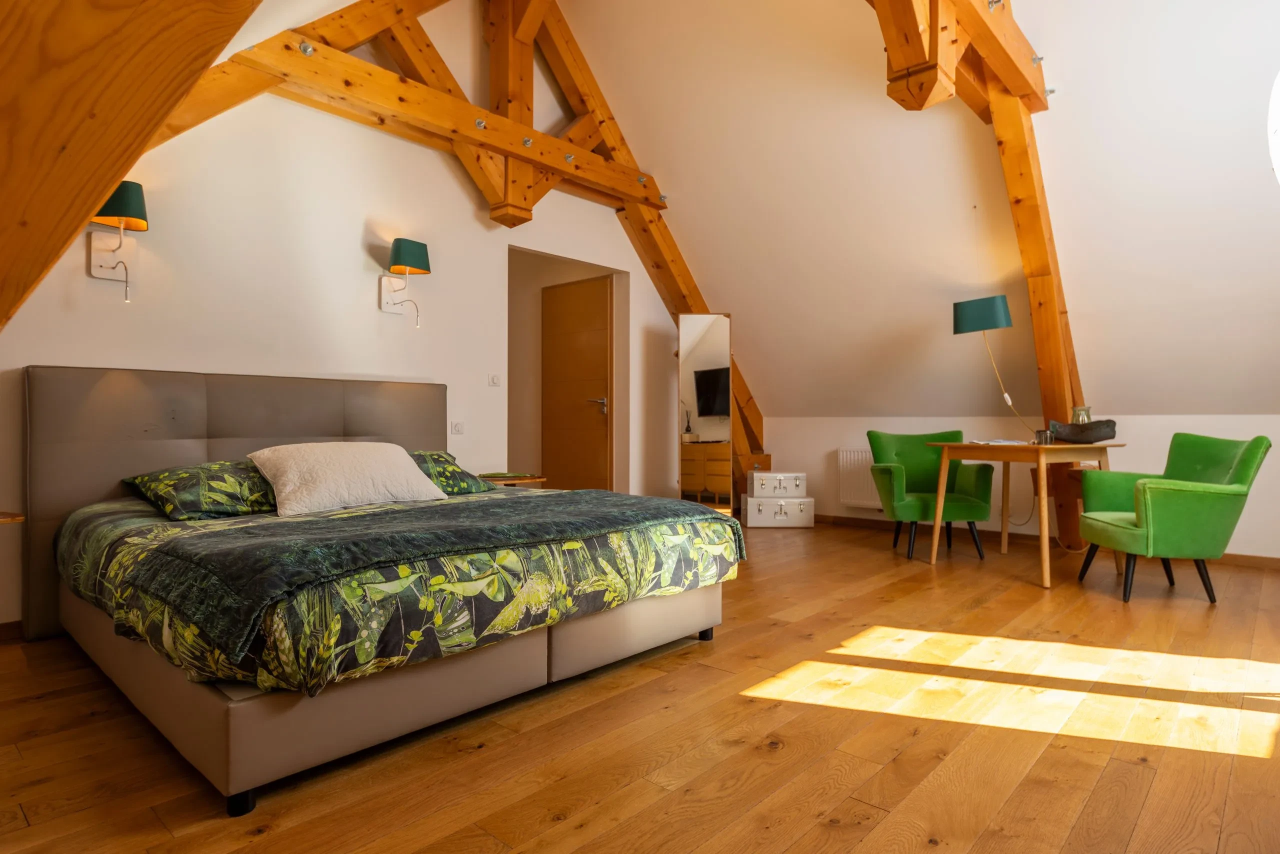 Chambre mansardée lumineuse avec lit double et fauteuils verts